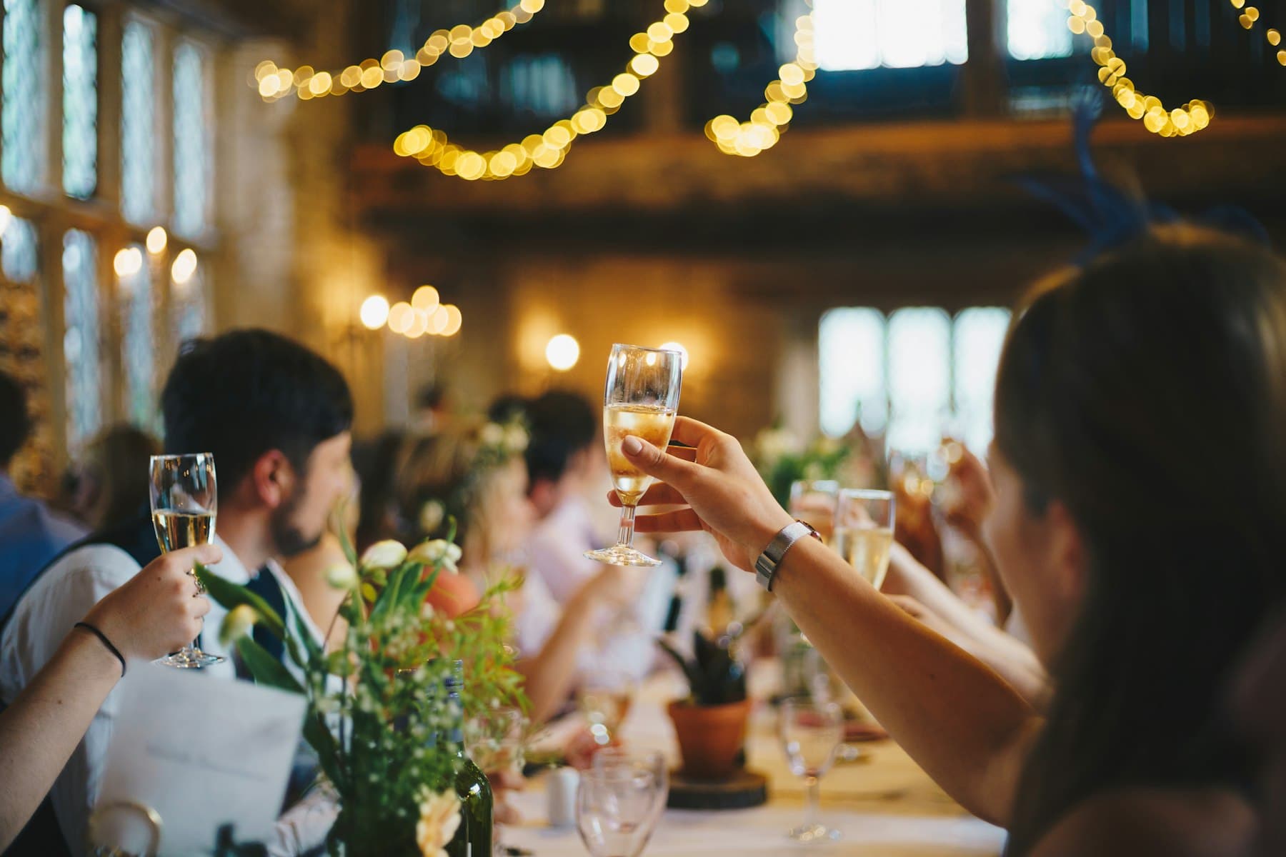 Wedding guests raising champagne glasses under string lights